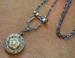 This free jewelry project by Rings & Things uses bezel cups, jewelry grade concrete (EnCapture Artisan Concrete), Gilders Paste, rhinestone chain, vintage inspired filigree, black gunmetal chain and has a delicate flower bead as the center of the mini mosaic.